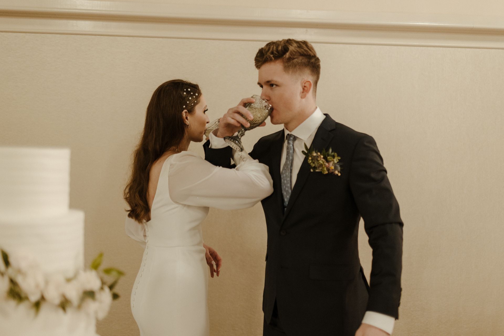 Newlyweds toast champagne; white cake, bride in long-sleeved dress, groom in suit.