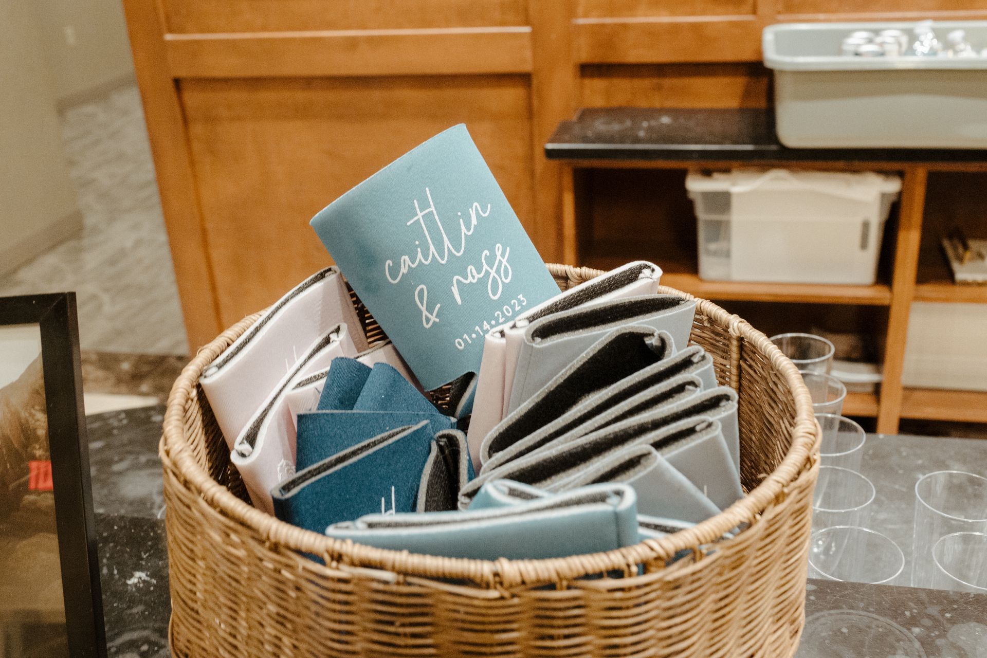 Basket of colorful folded fabric items, including a book, on a table. Wooden cabinets are in the background.