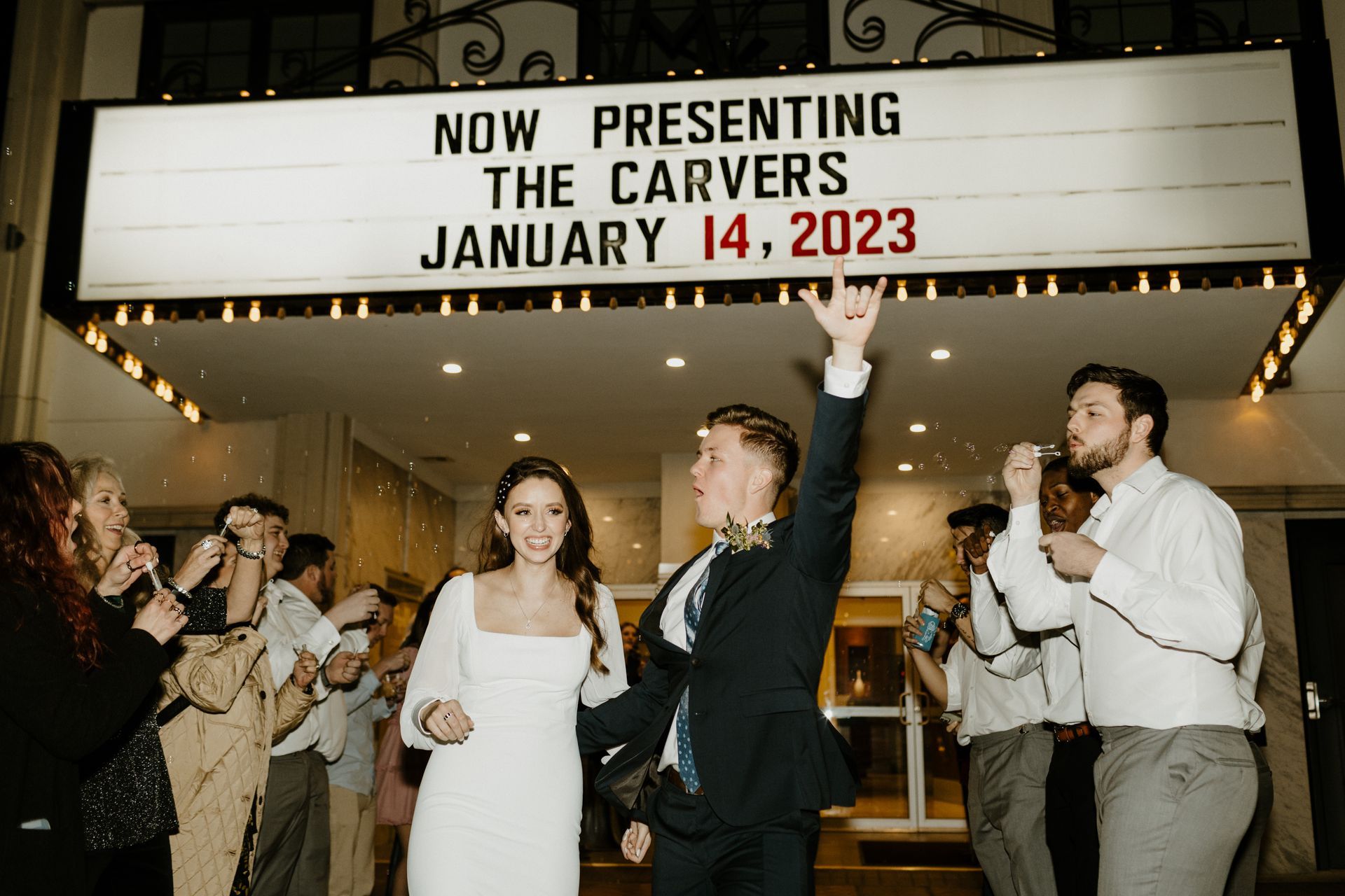 Newlyweds celebrate in front of a marquee reading 