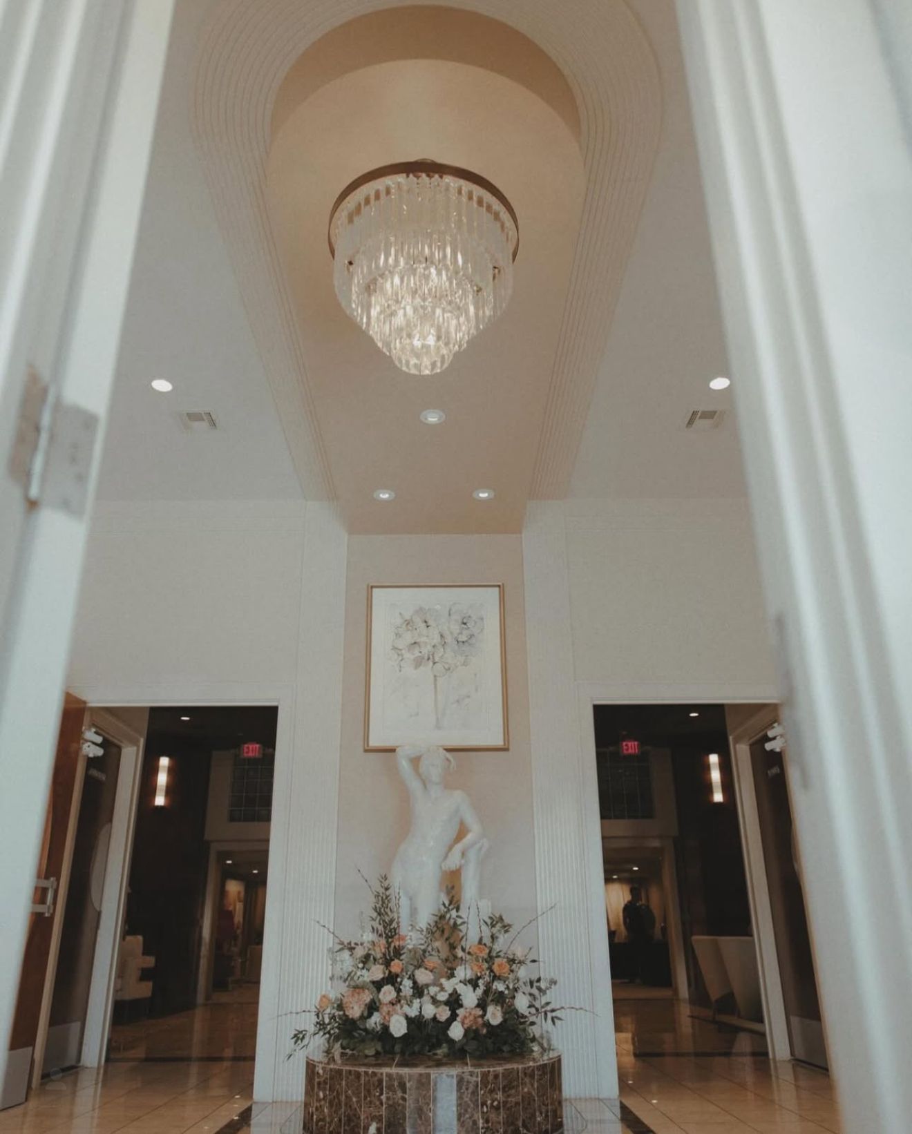 Elegant white lobby with chandelier, sculpture, and floral arrangement.
