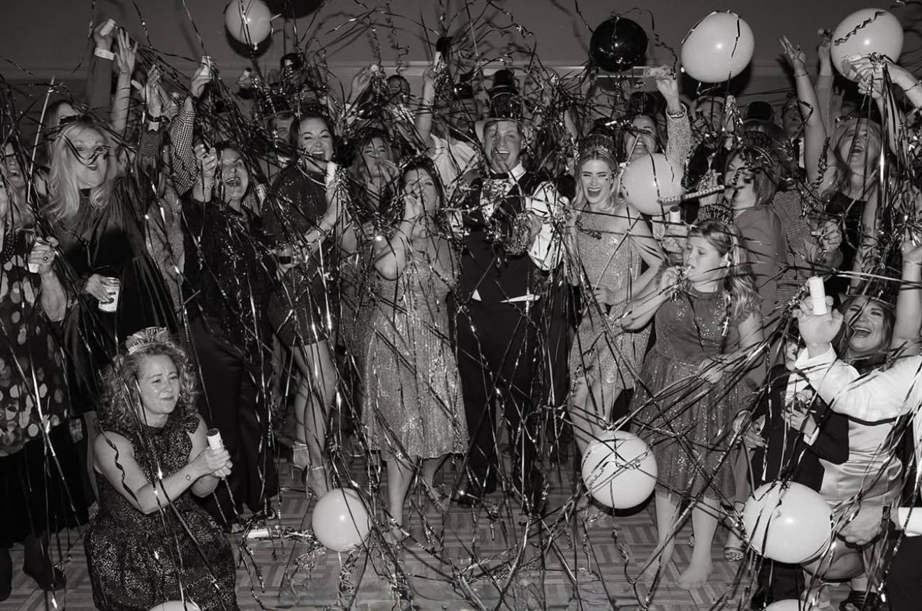 People celebrating, confetti and balloons flying in a crowded room.