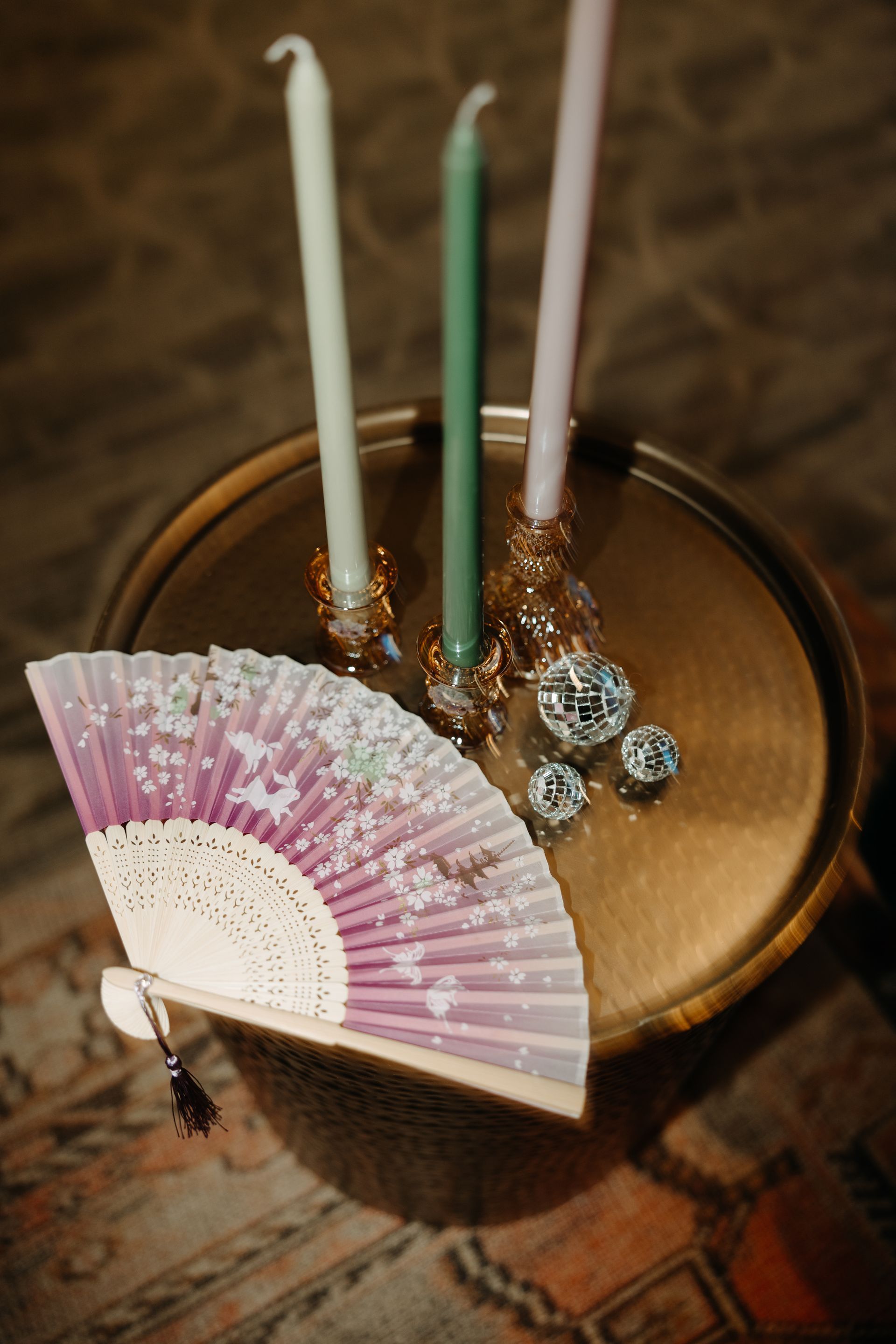 A round gold tray with candles, decorative balls, and a purple fan.