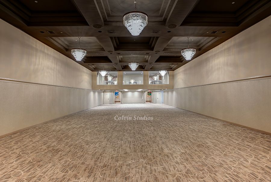 Empty rectangular event space with carpeted floor, high ceiling, and large chandeliers.