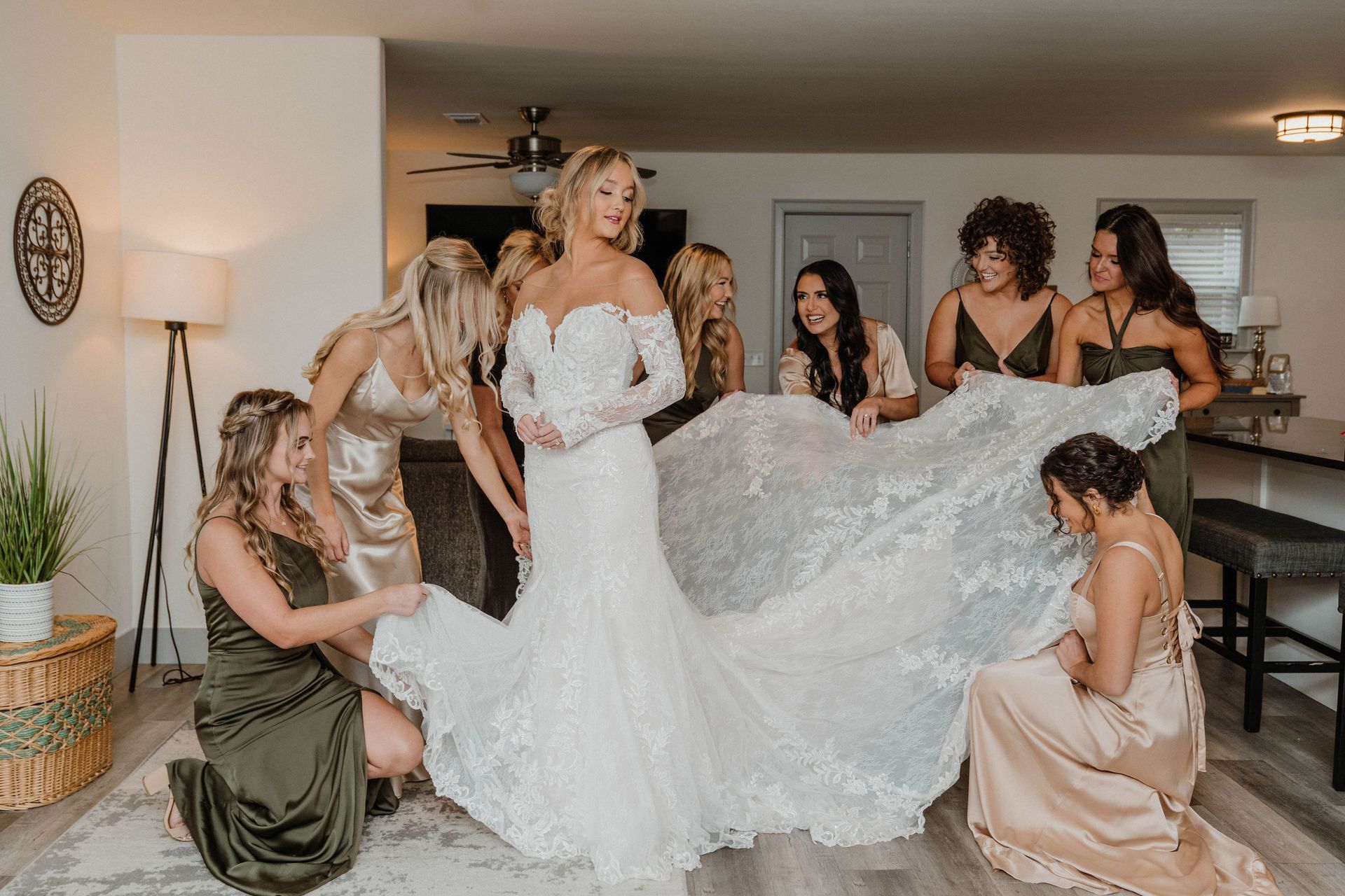 Bride in a white gown surrounded by bridesmaids in different colored dresses, assisting with the train.
