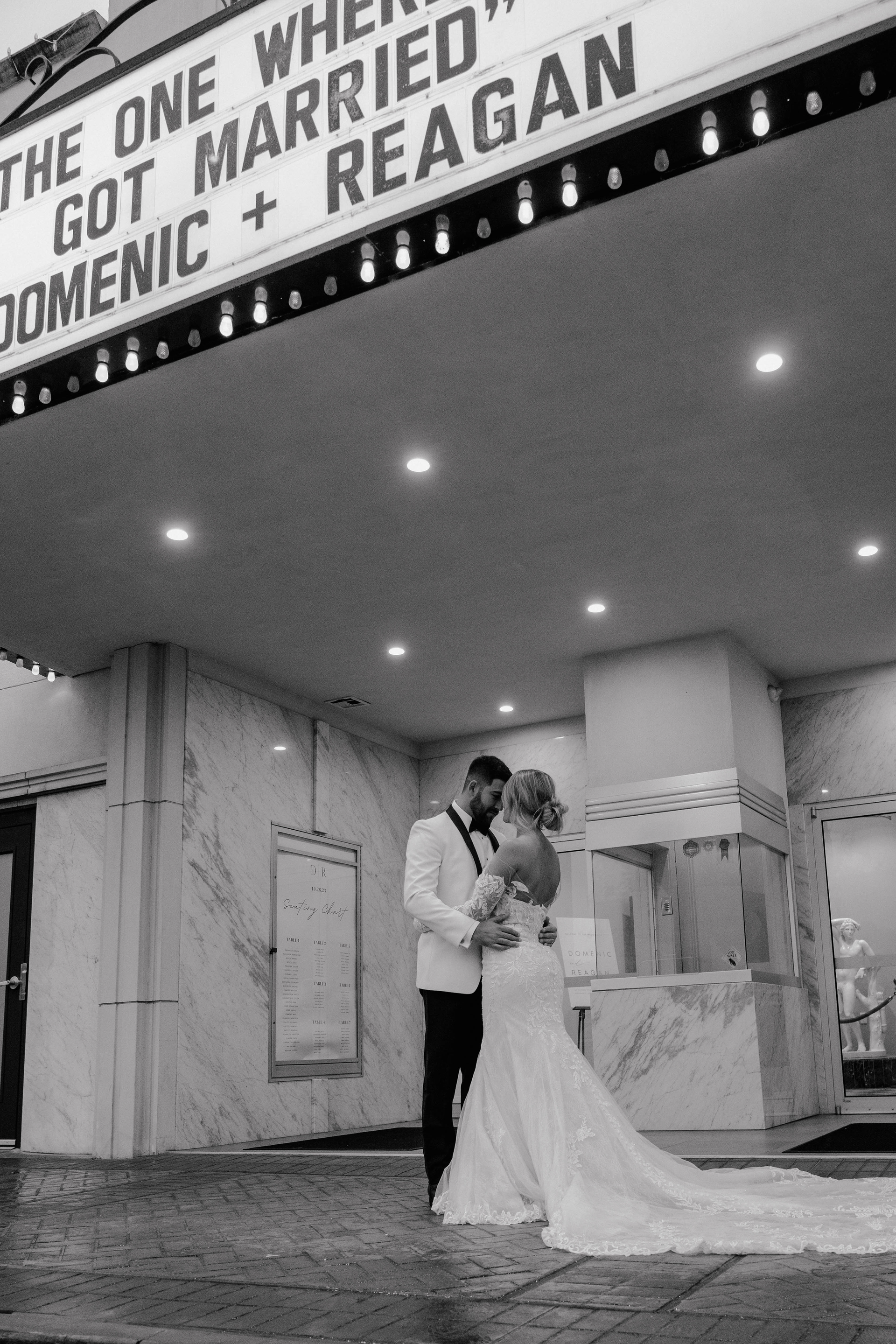 Newlyweds embrace under a marquee that reads, 