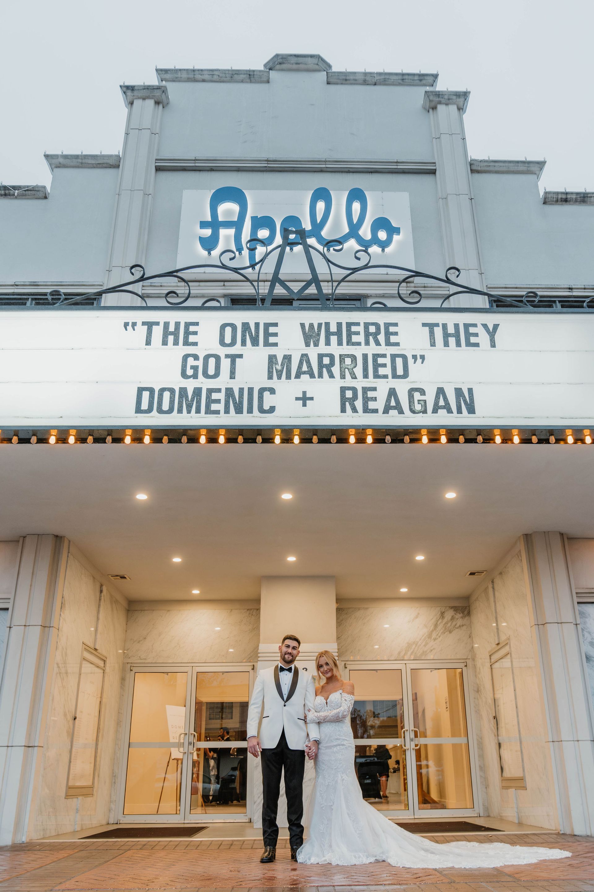 Couple in wedding attire posing in front of the Apollo Theater marquee with 