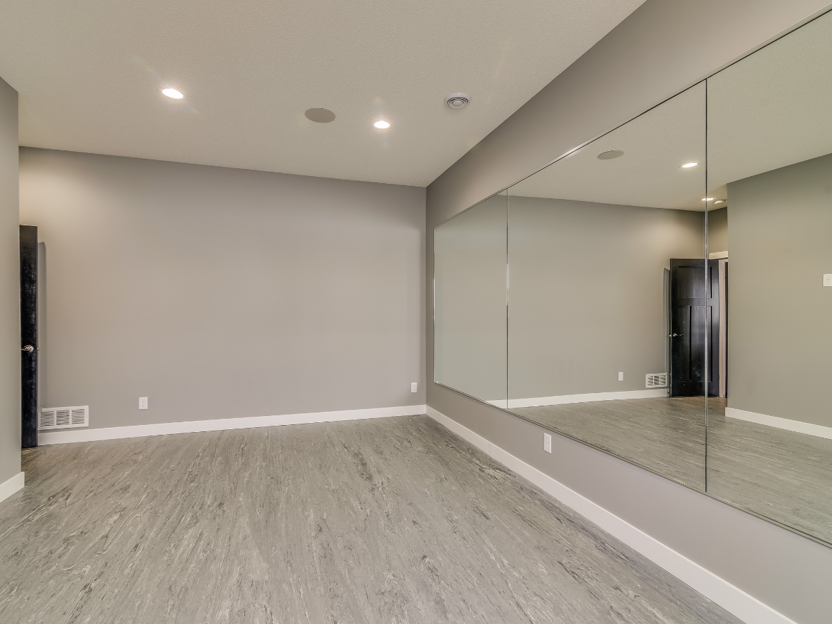 Empty room with gray walls, large mirror, and gray flooring.