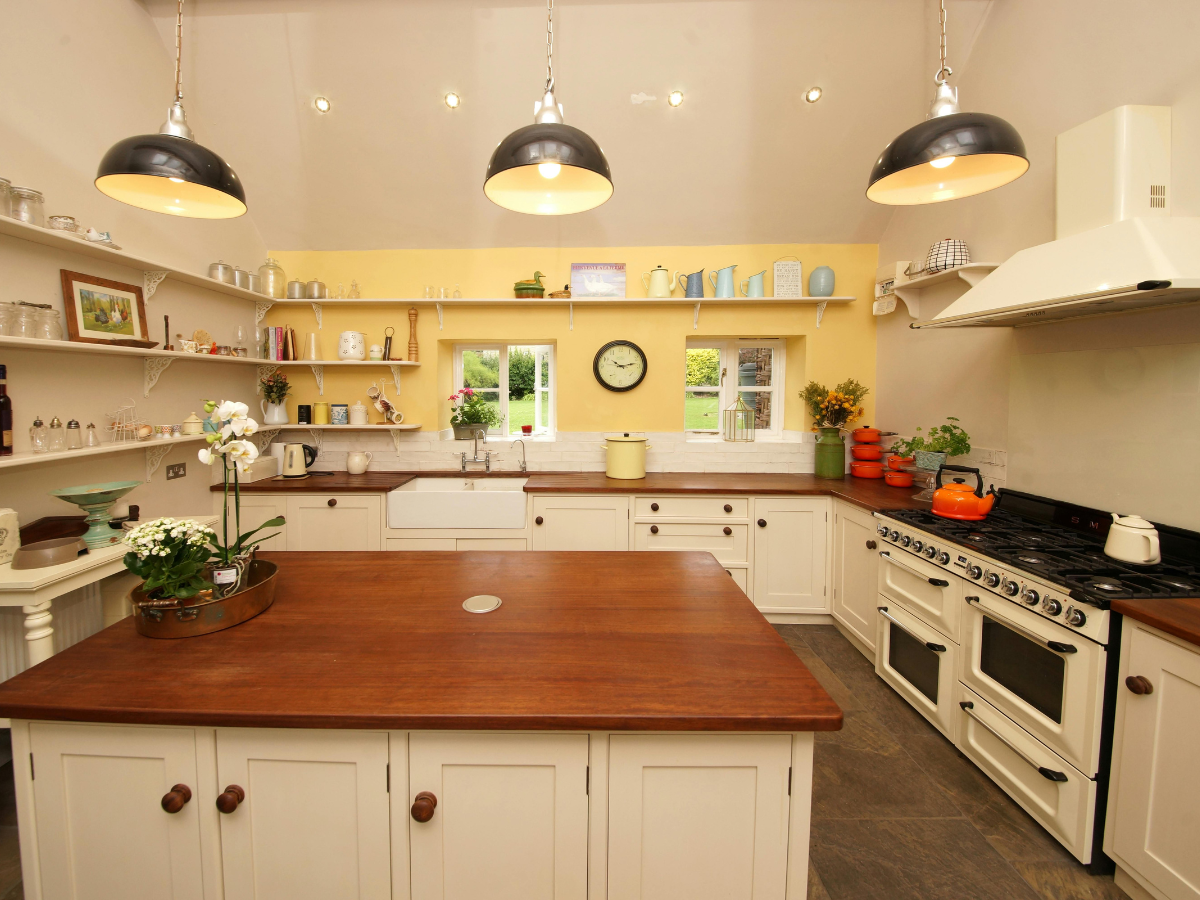 Cream-colored kitchen with yellow accent wall, wood countertops, island, and industrial pendant lights.