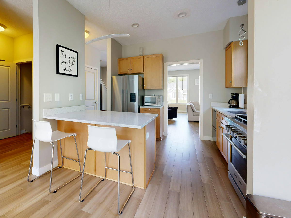 Modern kitchen with a breakfast bar, stainless steel appliances, and wood flooring.