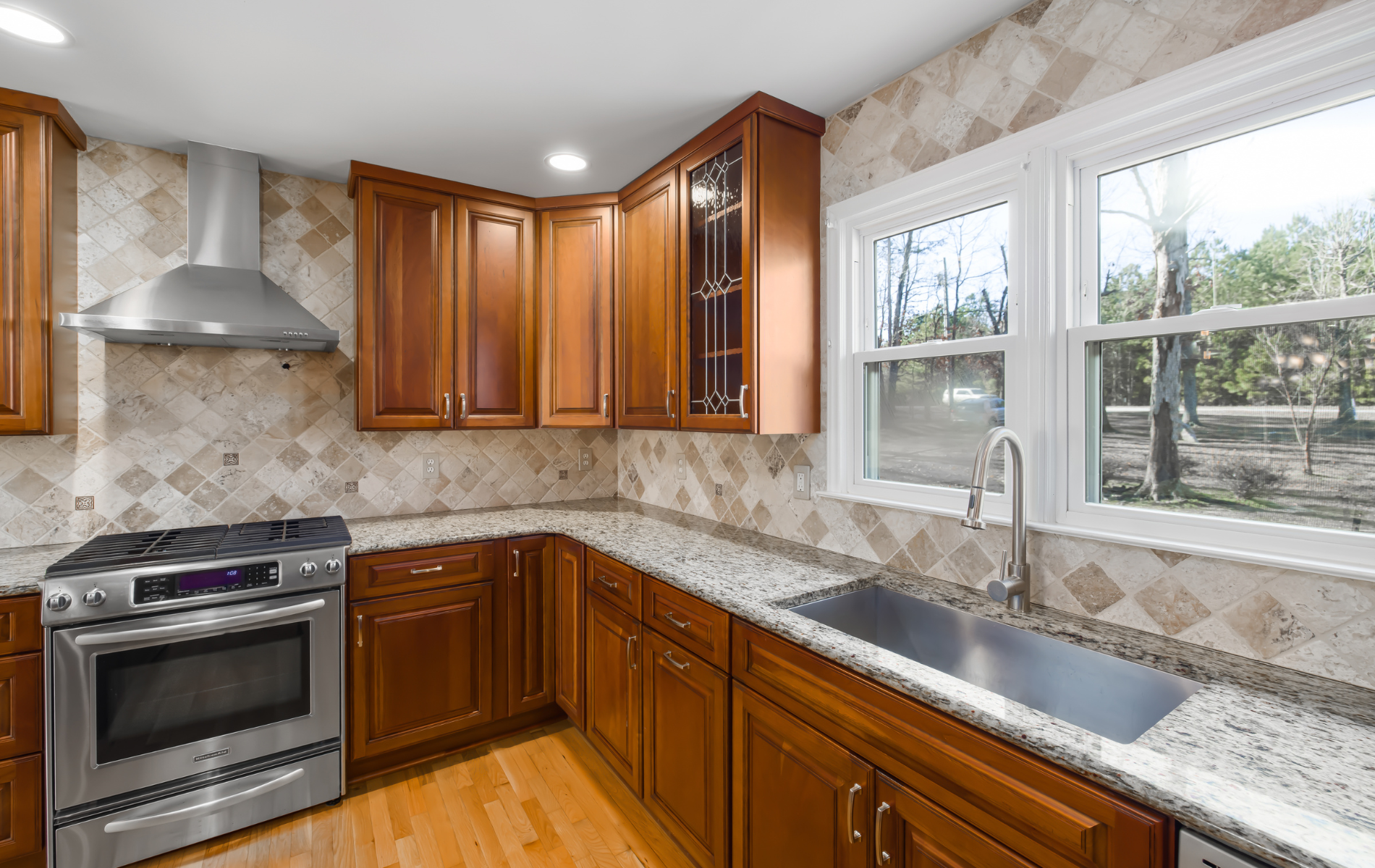Kitchen with wooden cabinets, stainless steel appliances, granite countertops, and tiled backsplash.