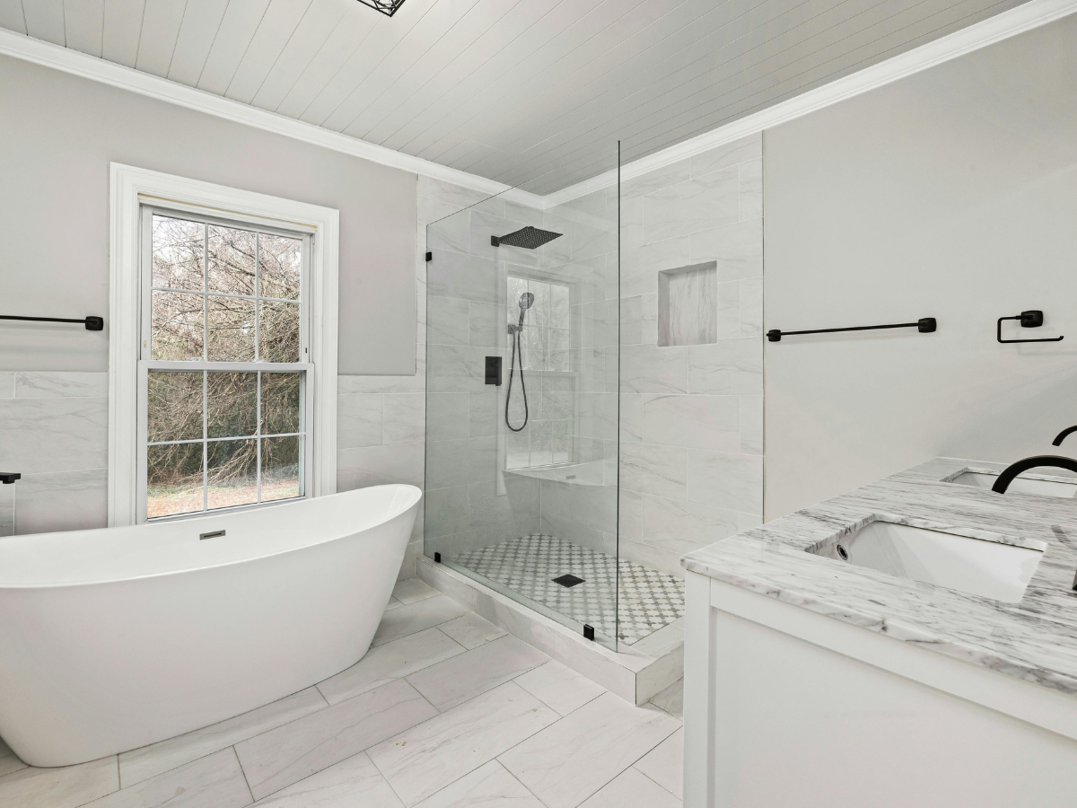Spacious, modern bathroom with a freestanding tub, glass shower, and marble countertops; neutral tones and natural light.