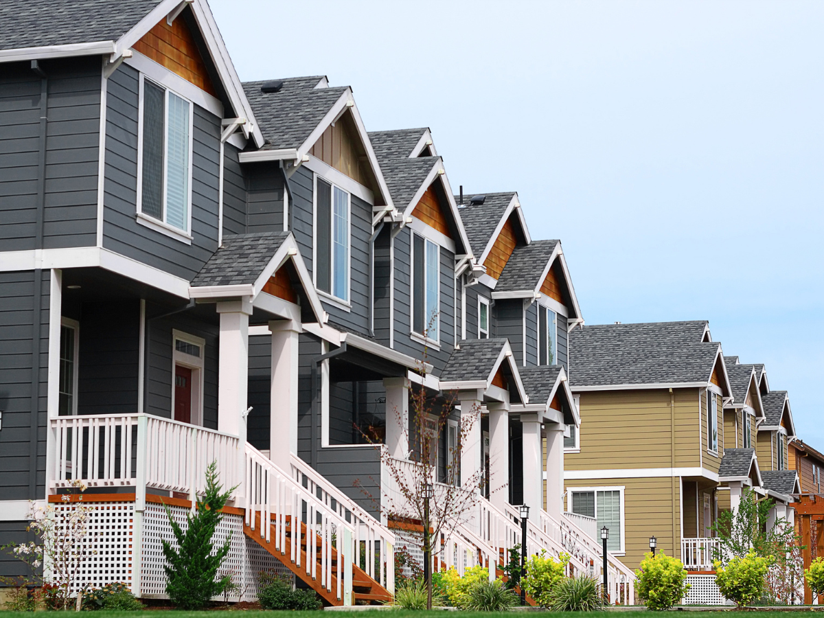 Row of townhouses with gray and tan siding, white trim, and matching gabled roofs.