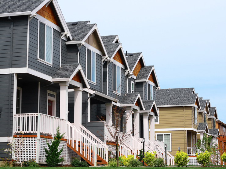 Row of townhouses with gray and tan siding, white trim, and matching gabled roofs.