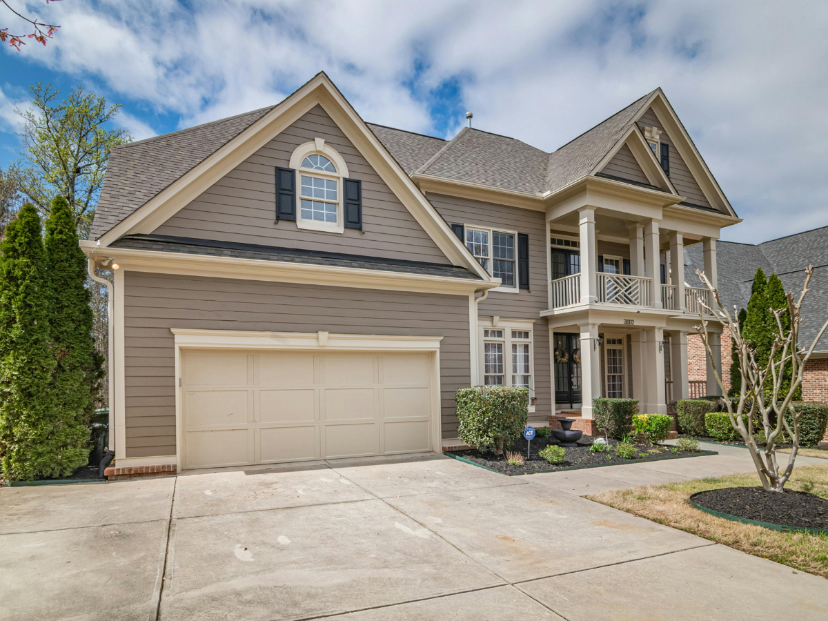Two-story beige house with a two-car garage, porch, and a gray roof.