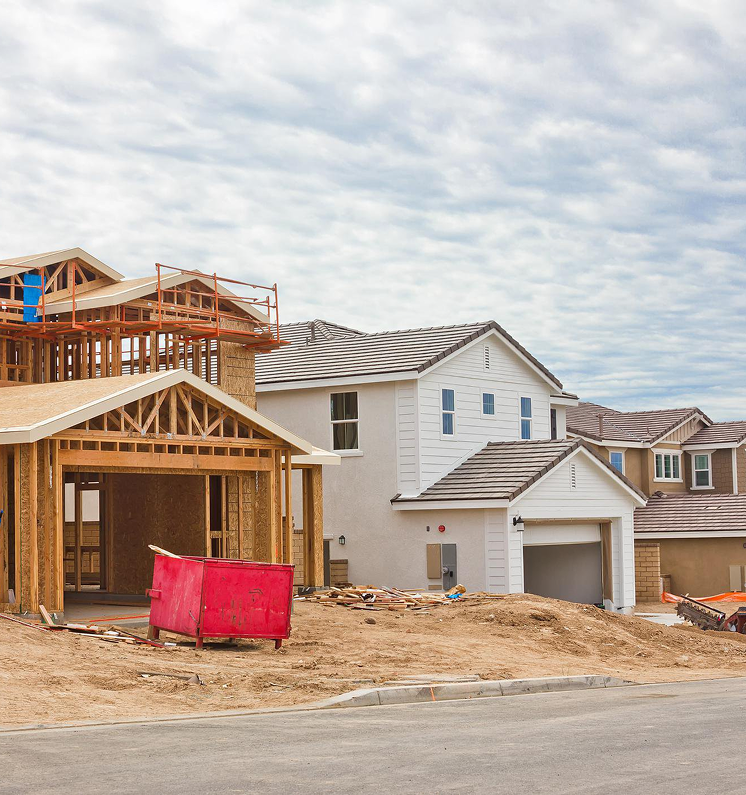 New houses under construction with exposed wooden frames and various stages of completion. Cloudy sky.