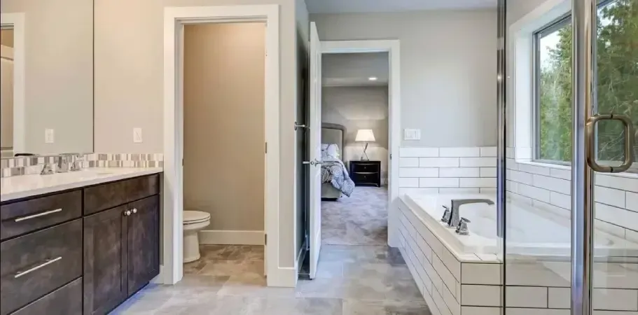 Bathroom with a dark vanity, toilet, tub, and shower. Doorway leads to a bedroom. Gray walls and flooring.