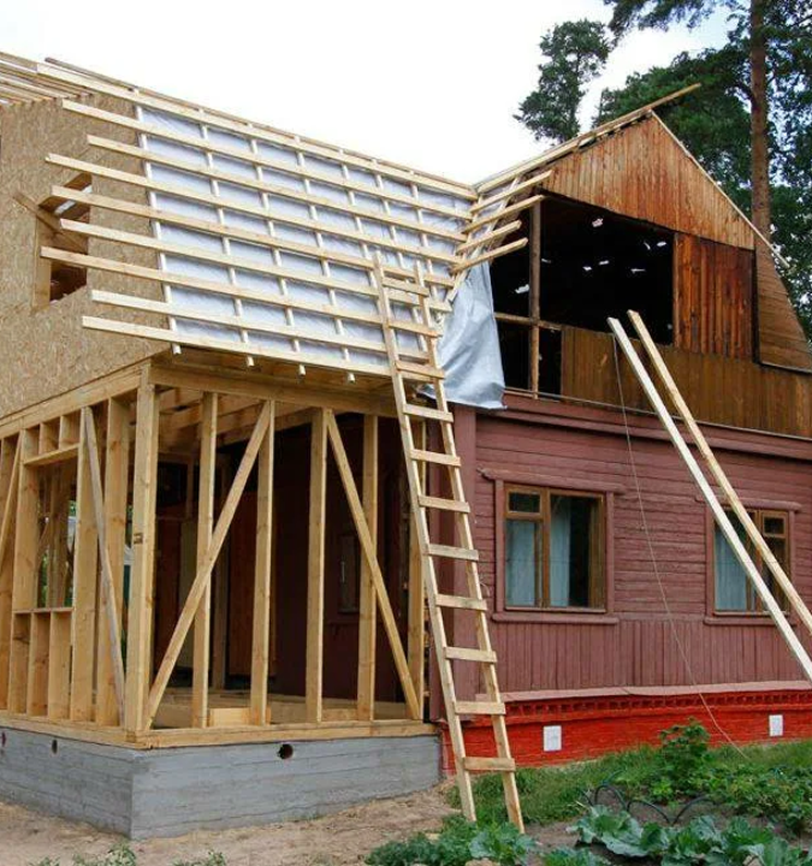 House under construction; wooden frame, ladders, red siding, unfinished roof.