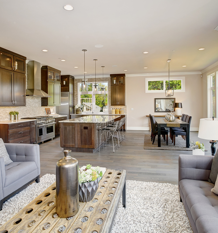 Open-concept kitchen and living area with dark wood cabinets, island, dining table, and gray sofas.