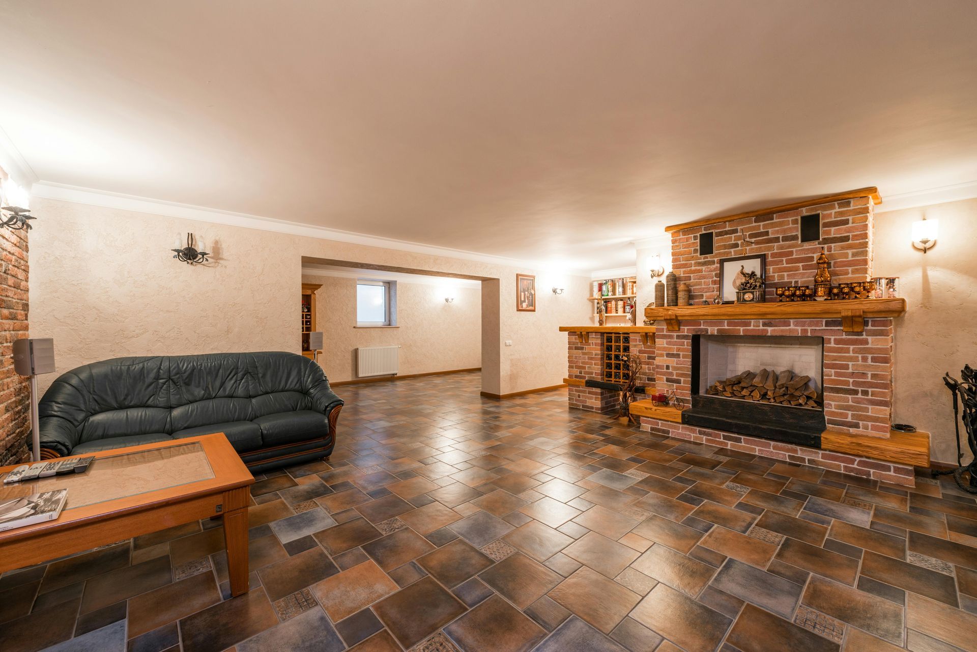 Spacious living room with dark sofa, brick fireplace, and tiled floor under warm lighting