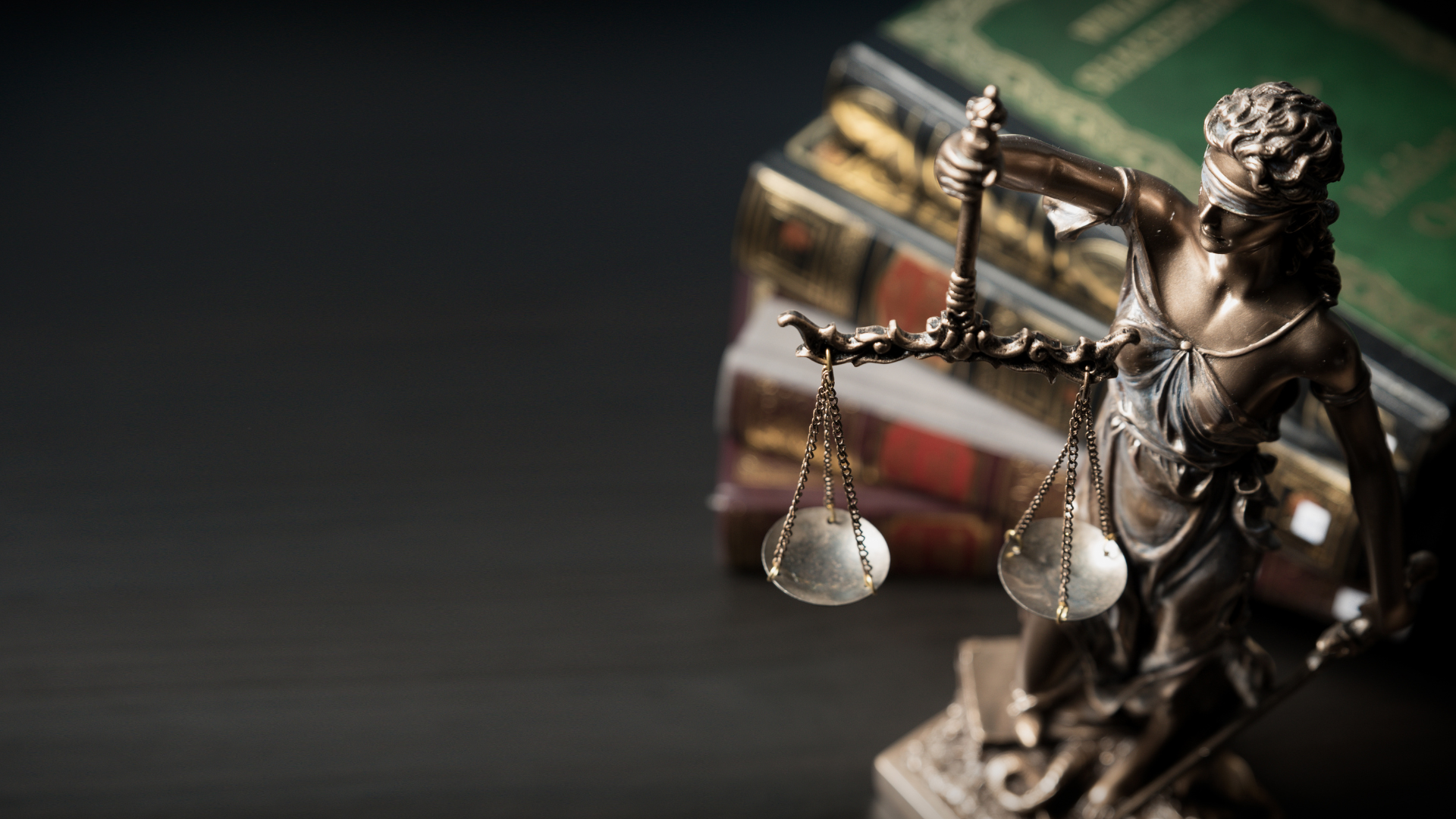 A statue of justice holding a scale in front of a stack of books.