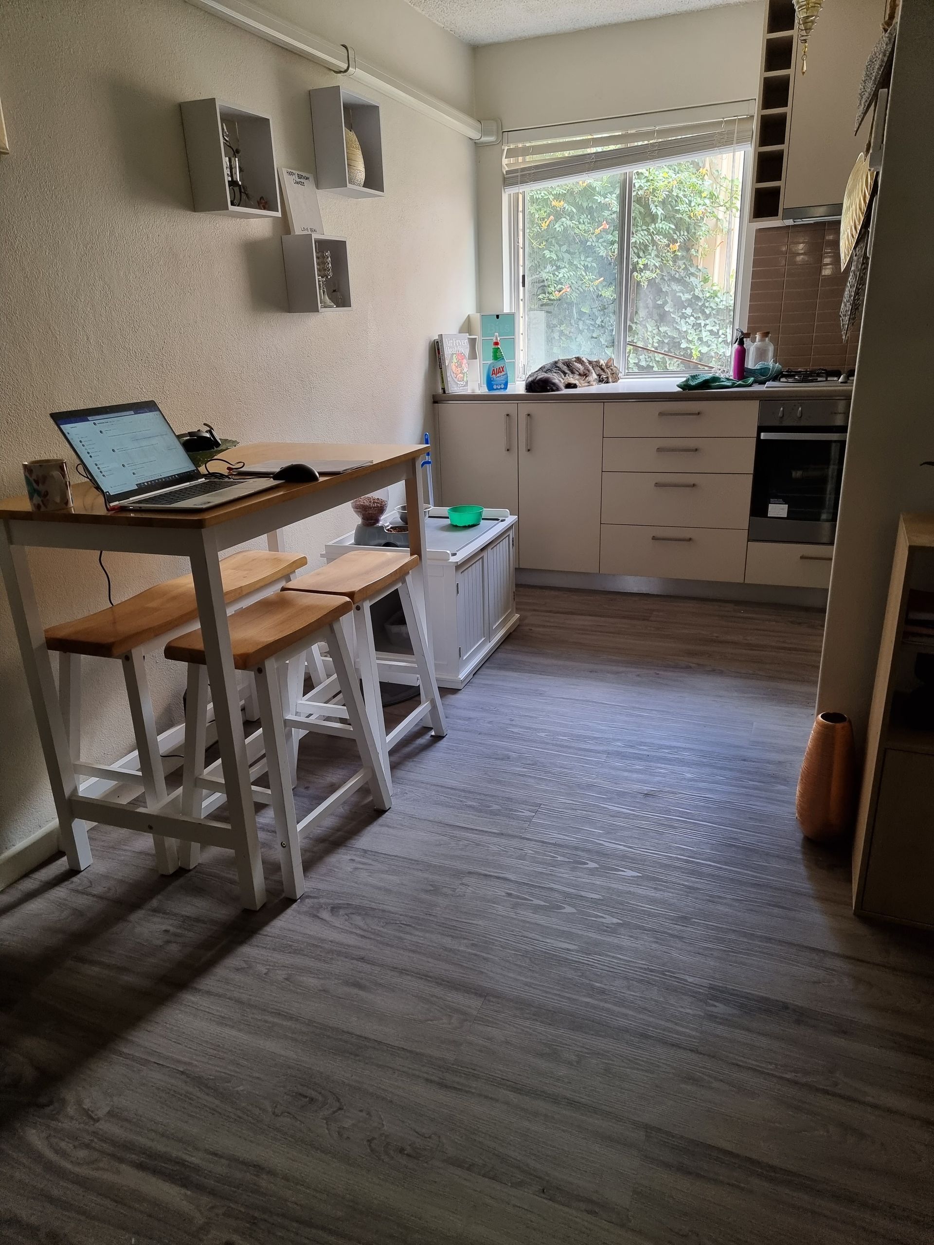 Kitchen With a Wooden Table, Open Laptop, White Cabinets, and a Sunlit Window — Queanbeyan Carpets in Queanbeyan, NSW