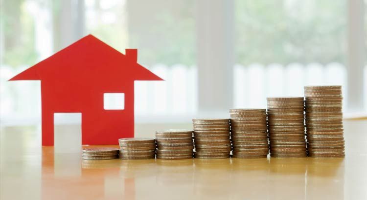 Red house cutout next to ascending stacks of coins, symbolizing home financial growth.