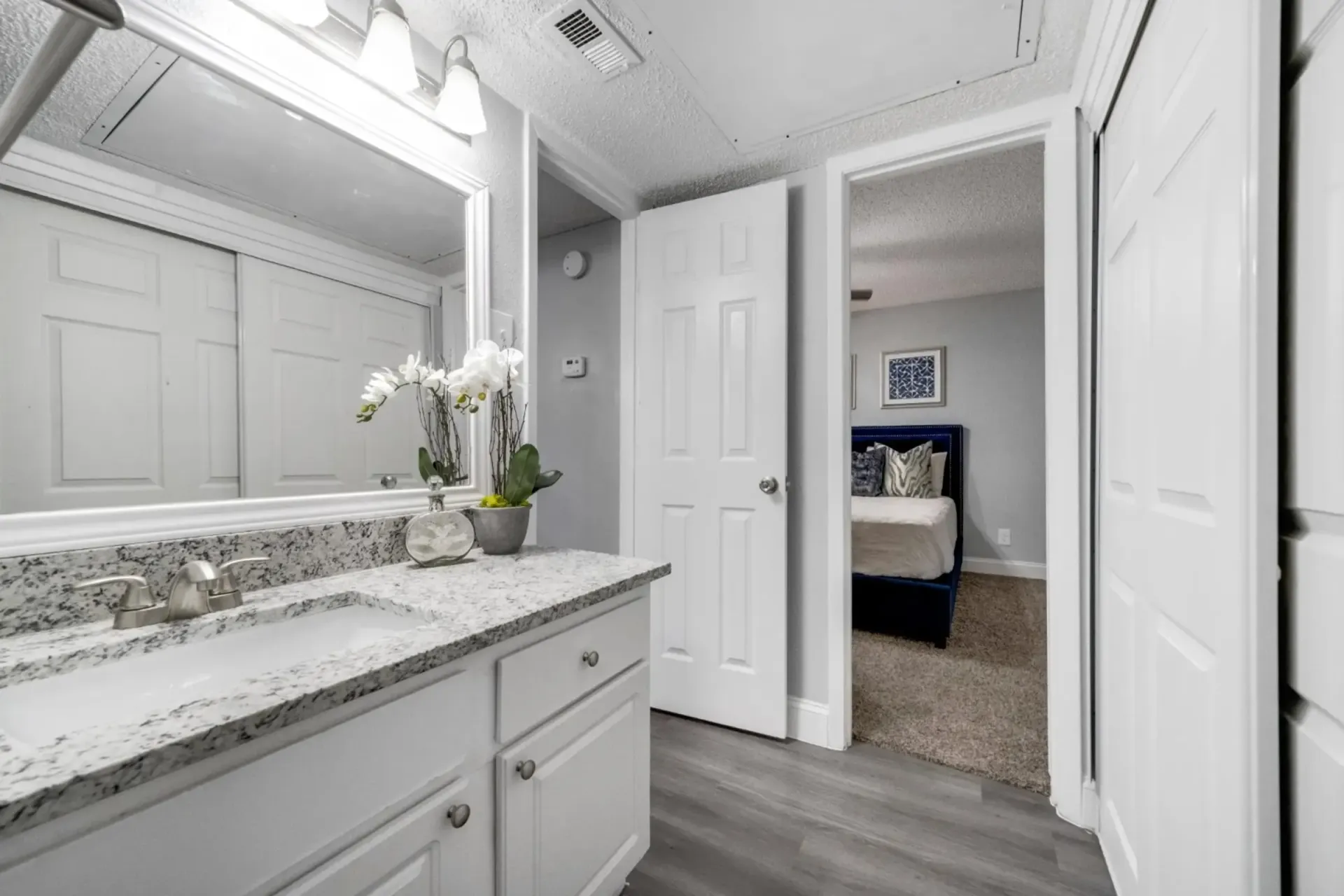 A bathroom with a sink , mirror , and cabinets leading to a bedroom.
