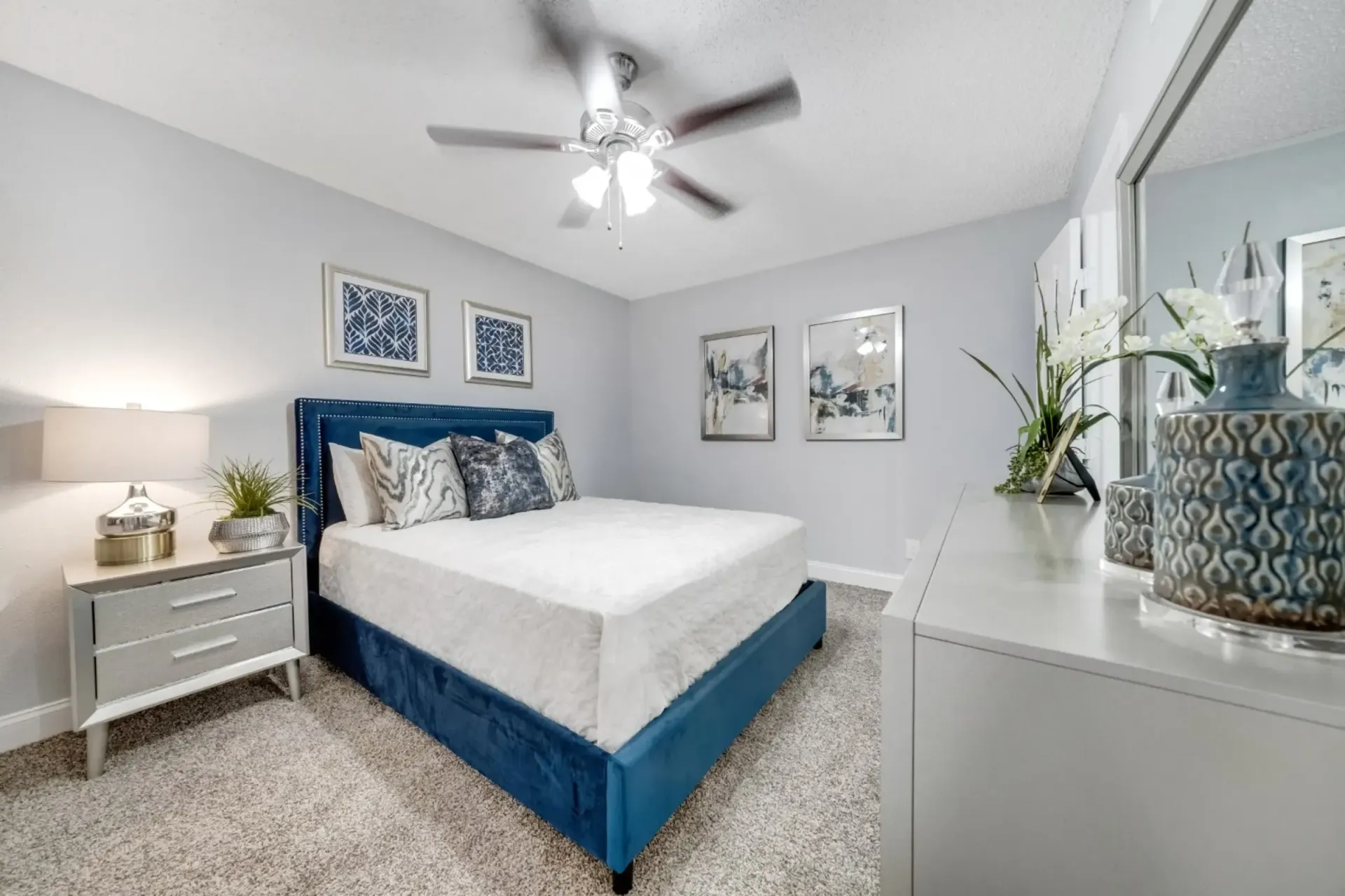 A bedroom with a bed , nightstand , mirror and ceiling fan.