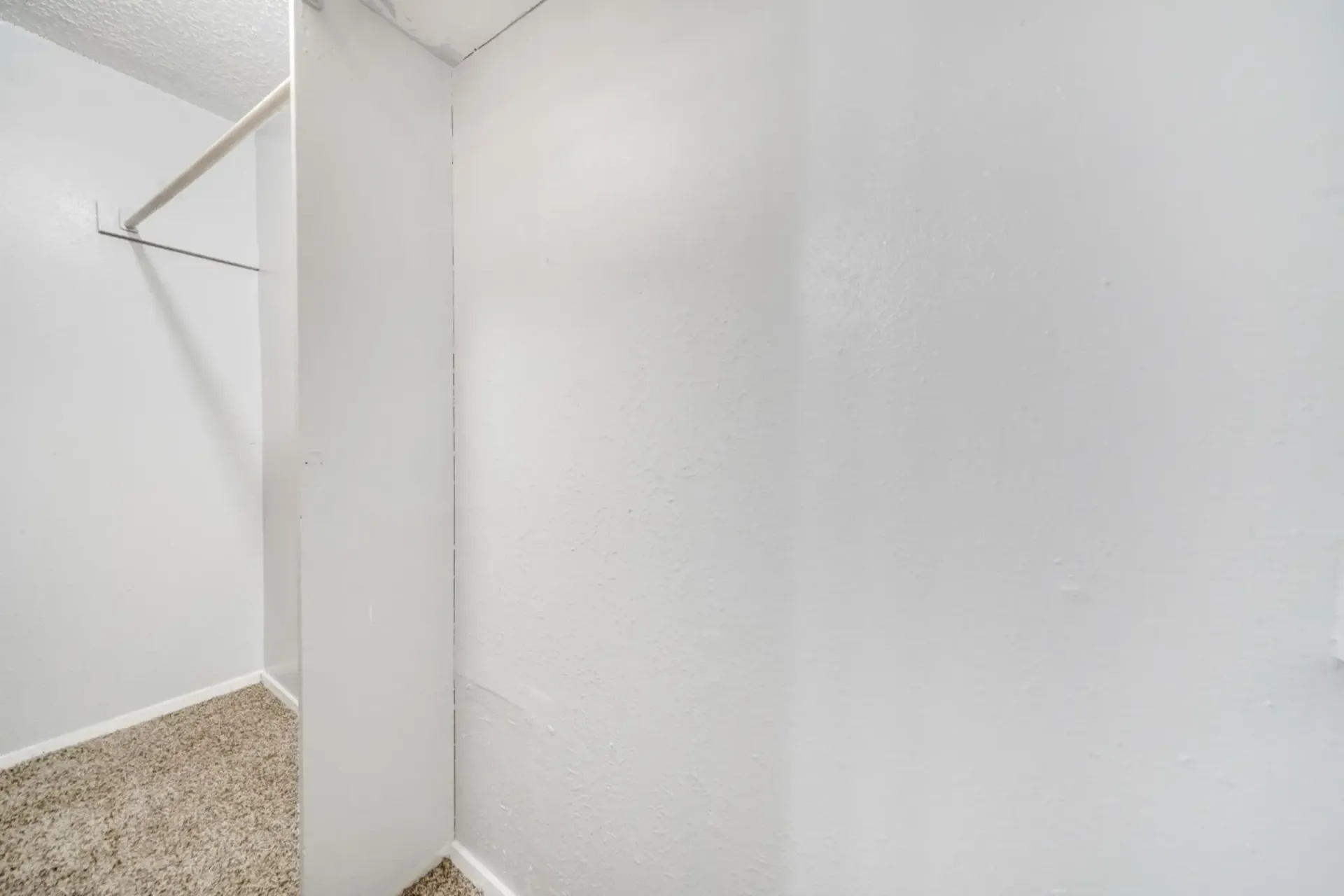 An empty walk in closet with a carpeted floor and white walls.