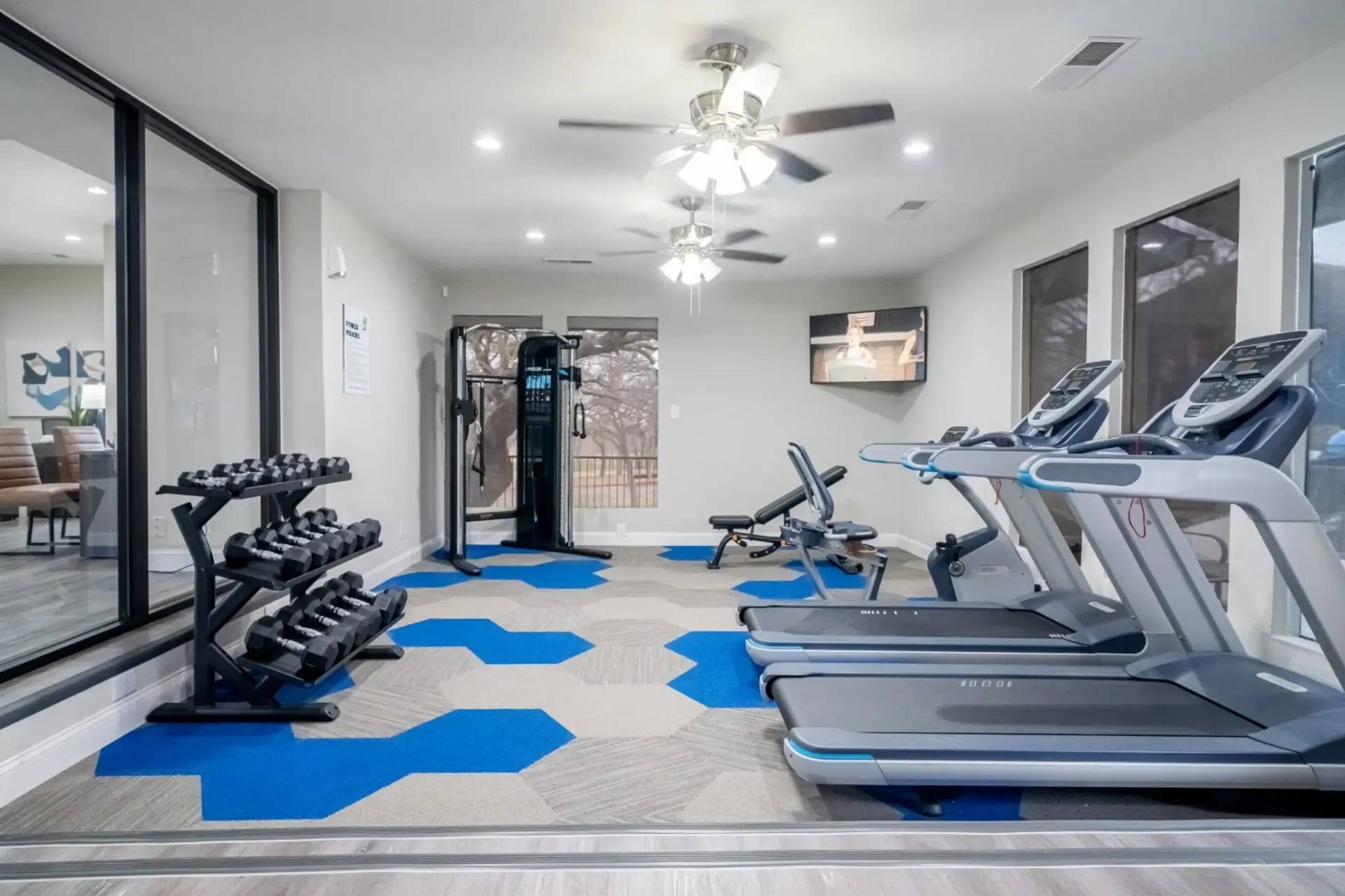 A gym with treadmills , dumbbells , and a television.