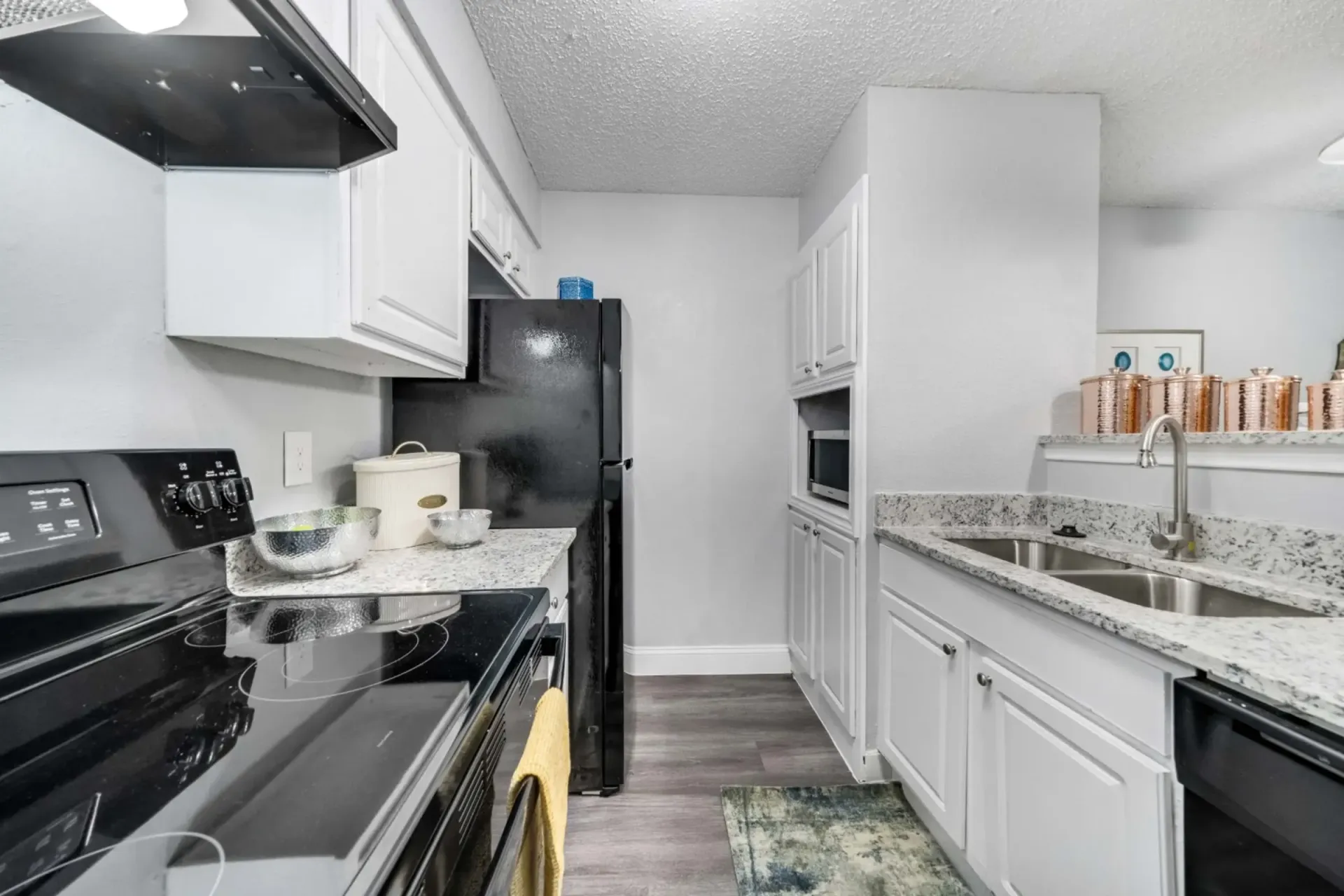 A kitchen with white cabinets , black appliances , a sink and a refrigerator.