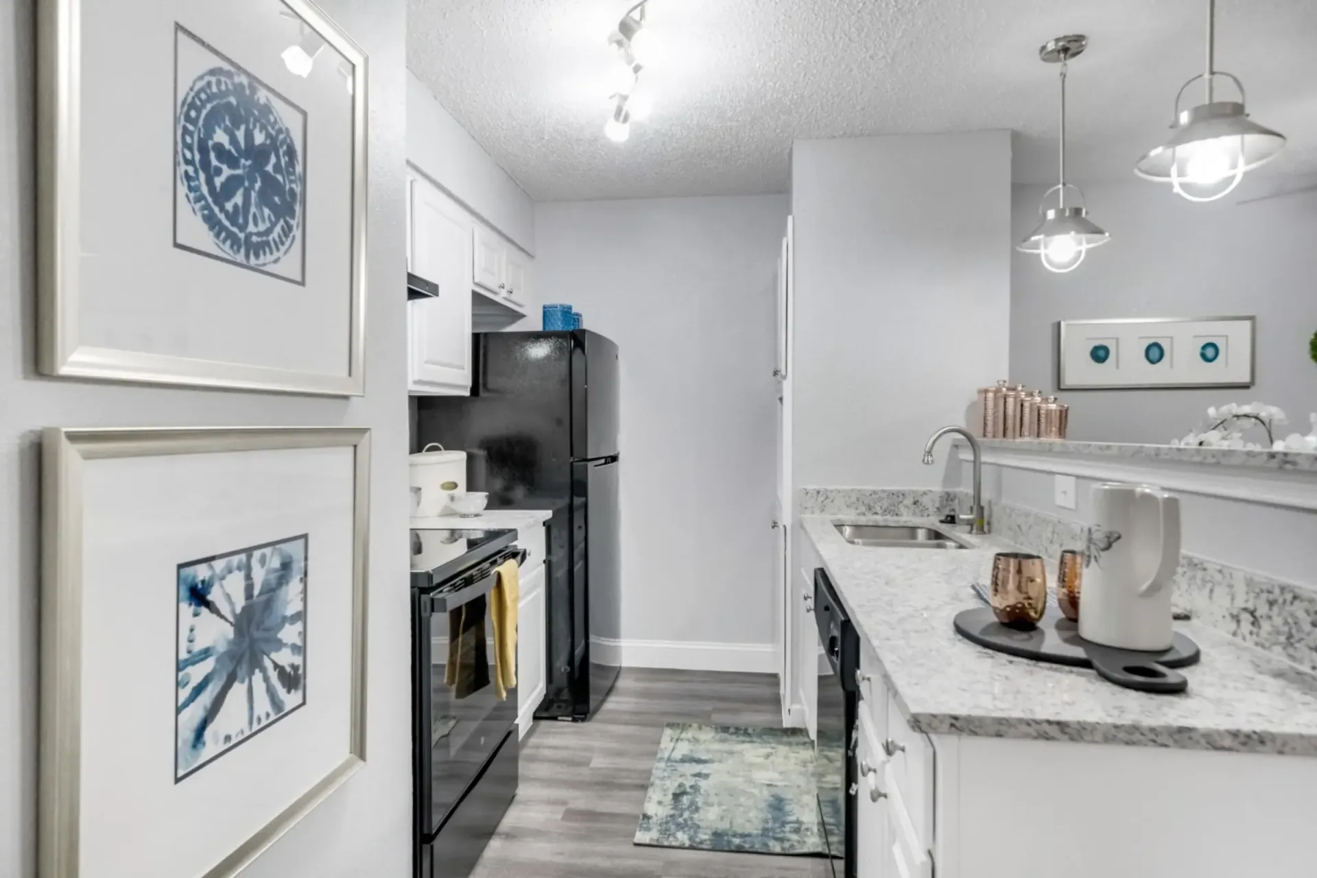 A kitchen with a refrigerator , stove , sink , and paintings on the wall.