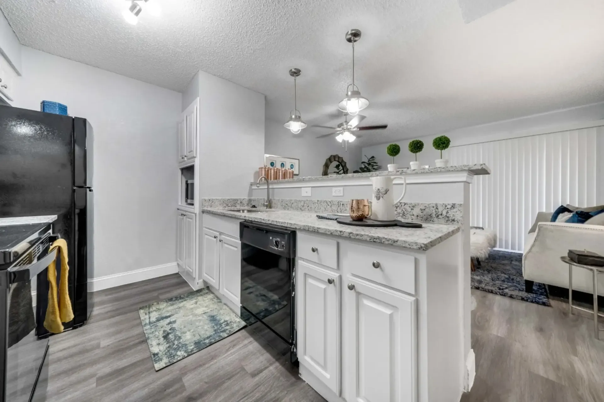 A kitchen with white cabinets , a black refrigerator , a stove , and a ceiling fan.