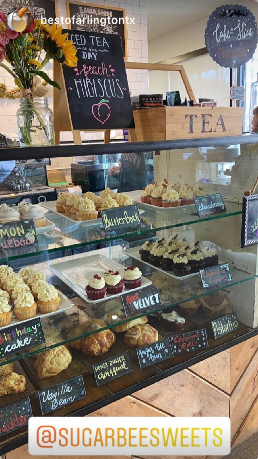 Bakery display case with baked goods: cupcakes, scones, and pastries. Chalkboard sign advertises iced tea.