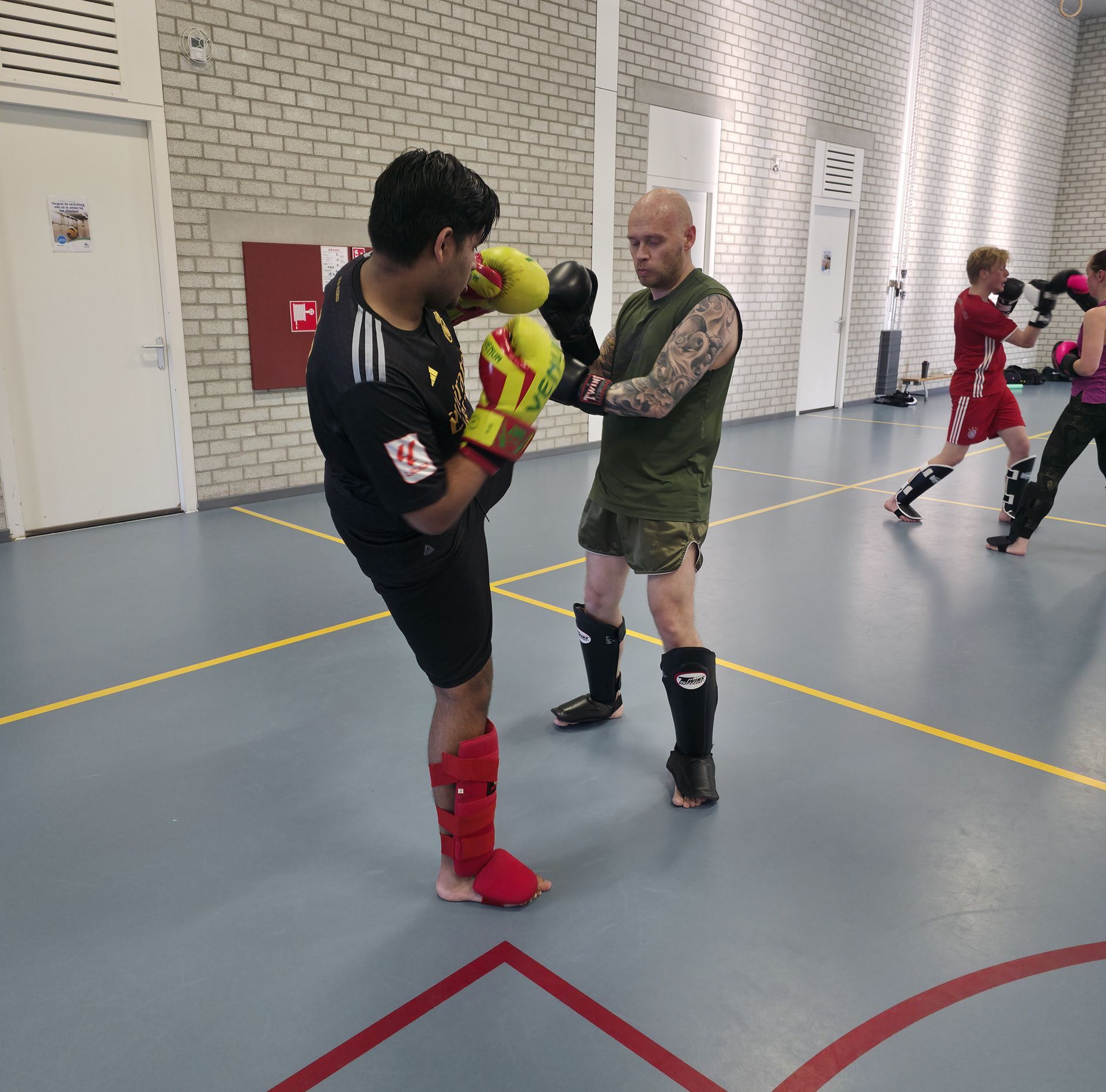 Two men practicing kickboxing indoors, one holding pads as the other throws a knee strike.