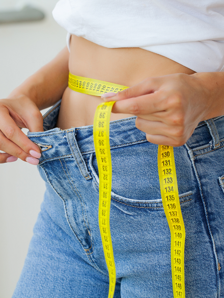 Measuring tape wrapped around a person’s waist over blue jeans to track waist size