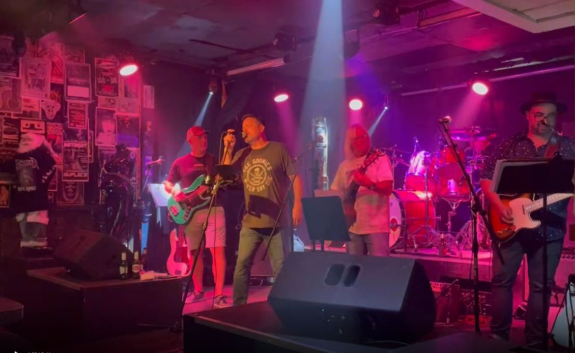 Band performing on stage with red and purple lights.