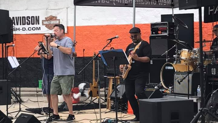 A band performing on stage at an outdoor event, with the lead singer at the mic and a bassist playing.