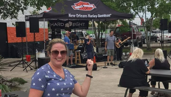 Woman in front of a band playing under a Harley-Davidson tent. People are sitting at tables.