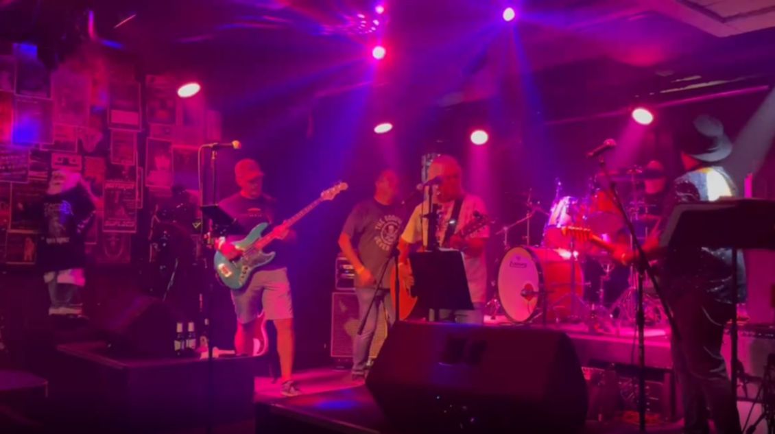 Band performing on stage under purple and white lights.