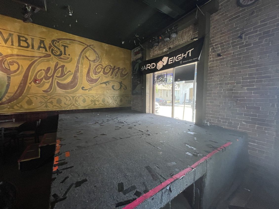 Inside a bar, a raised stage faces a mural reading 