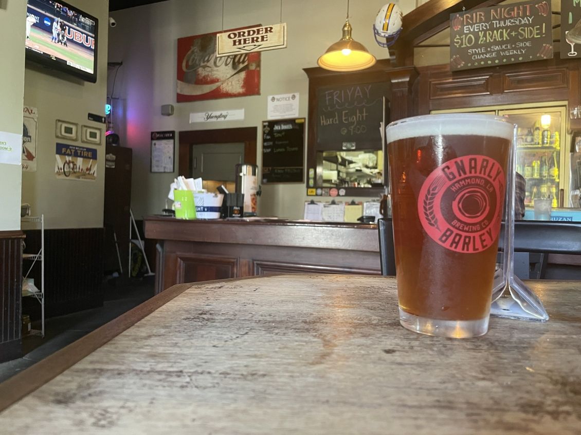 A glass of beer with the Gnarly Barley logo on a wooden bar in a bar setting.
