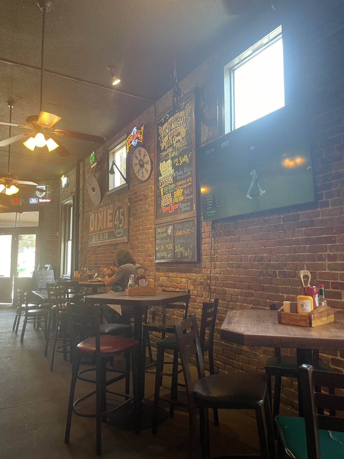 Interior of a bar with brick walls, tables, chairs, and a TV. Some patrons are present.