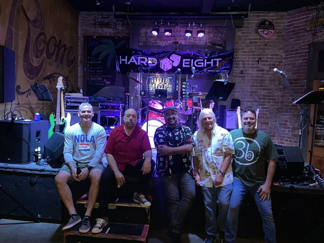 Five band members pose on stage in front of a banner that reads 