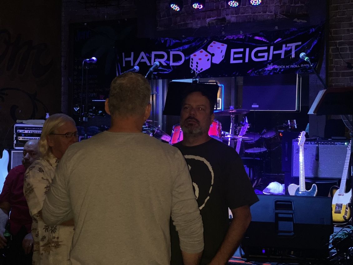 Two men talking in front of a stage with band equipment and a 