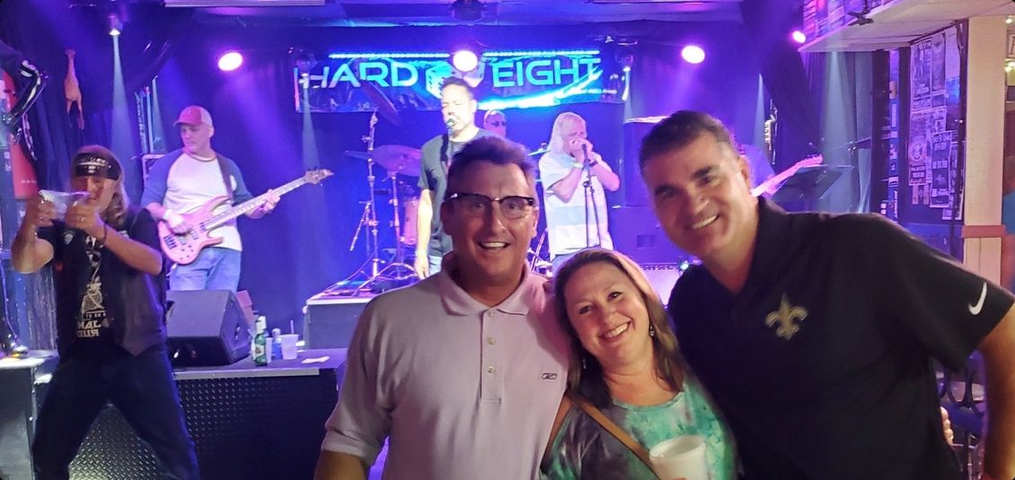 People smiling, posing with a band on stage, neon sign 