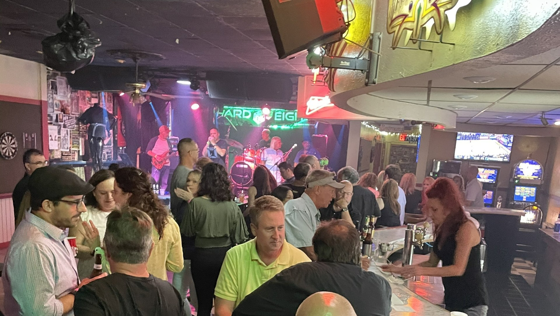 Bar scene with a live band performing, patrons enjoying drinks, and a bartender serving.