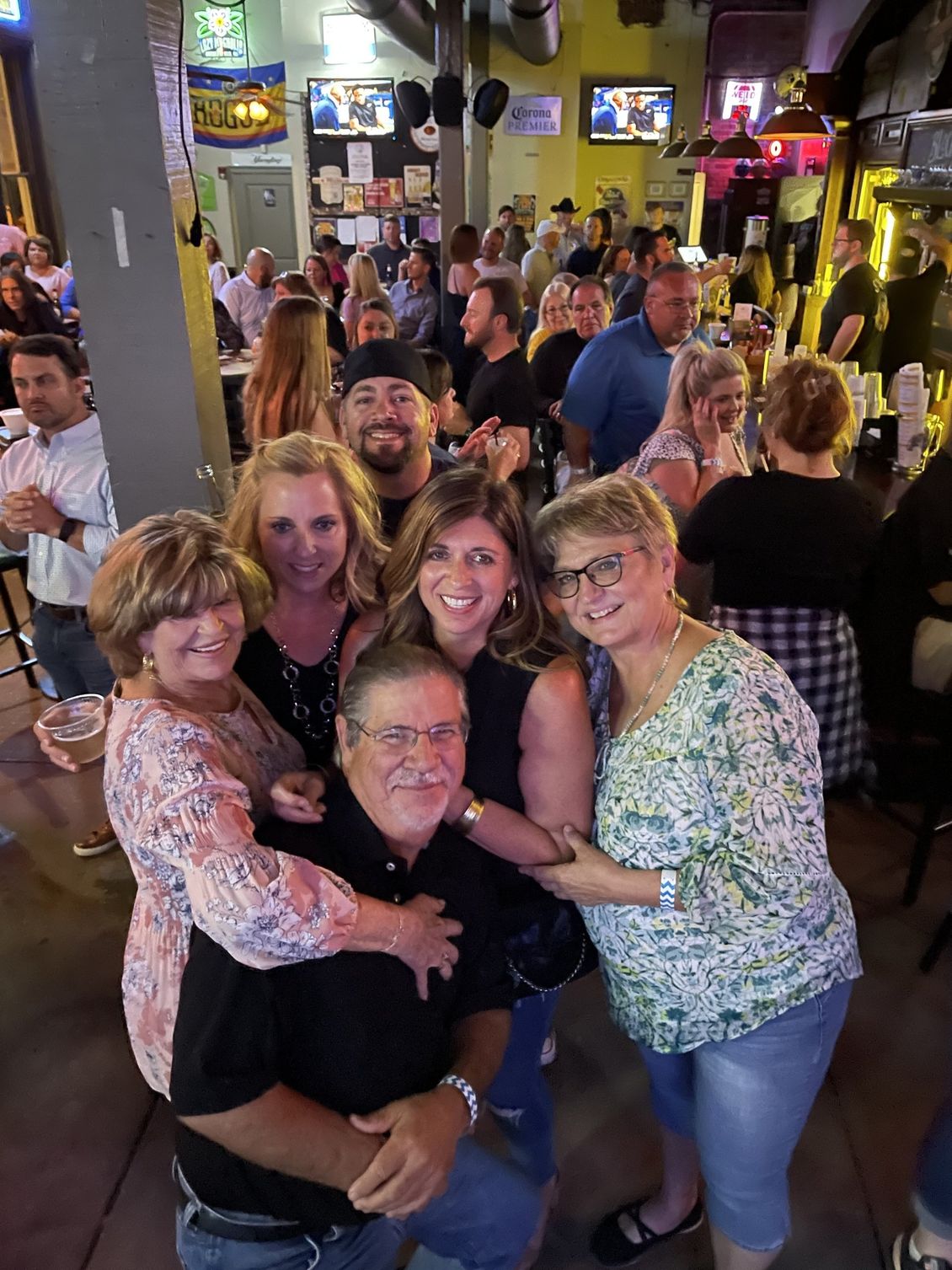 Group of people smiling and posing in a crowded bar.