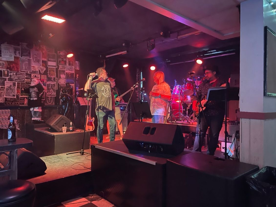 Band performing on a dimly lit stage in a bar, with the vocalist at center stage singing.