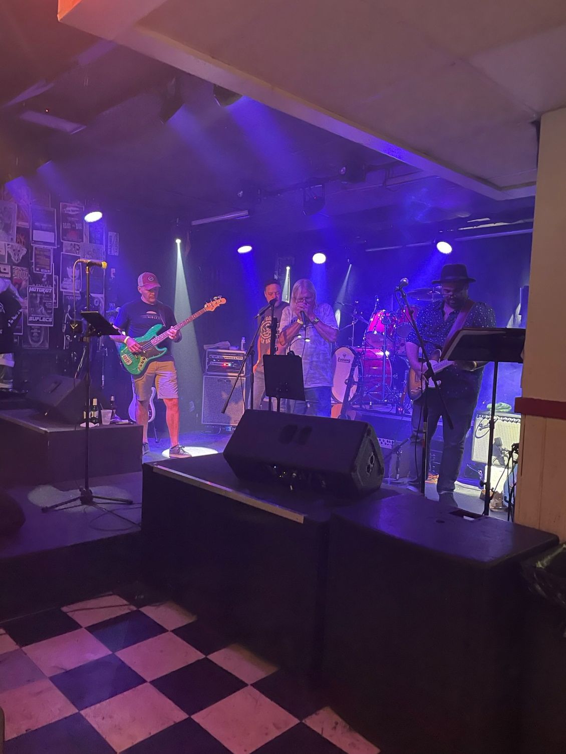 Band performing on stage under blue and white lights in a dimly lit venue.